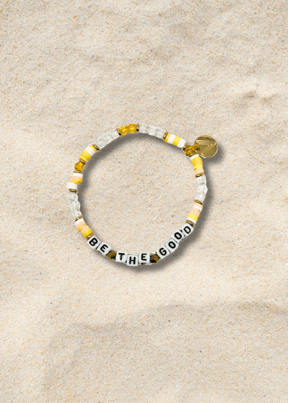 Bracelet with 'BE THE GOOD' message on a beige sand background